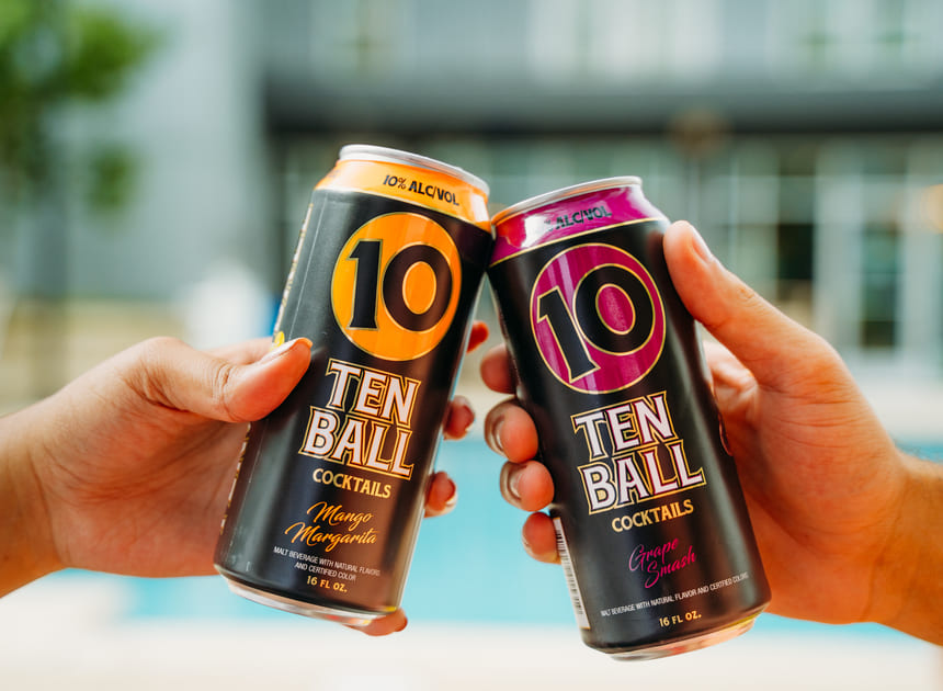 two hands holding tenball cocktails cans making a toast